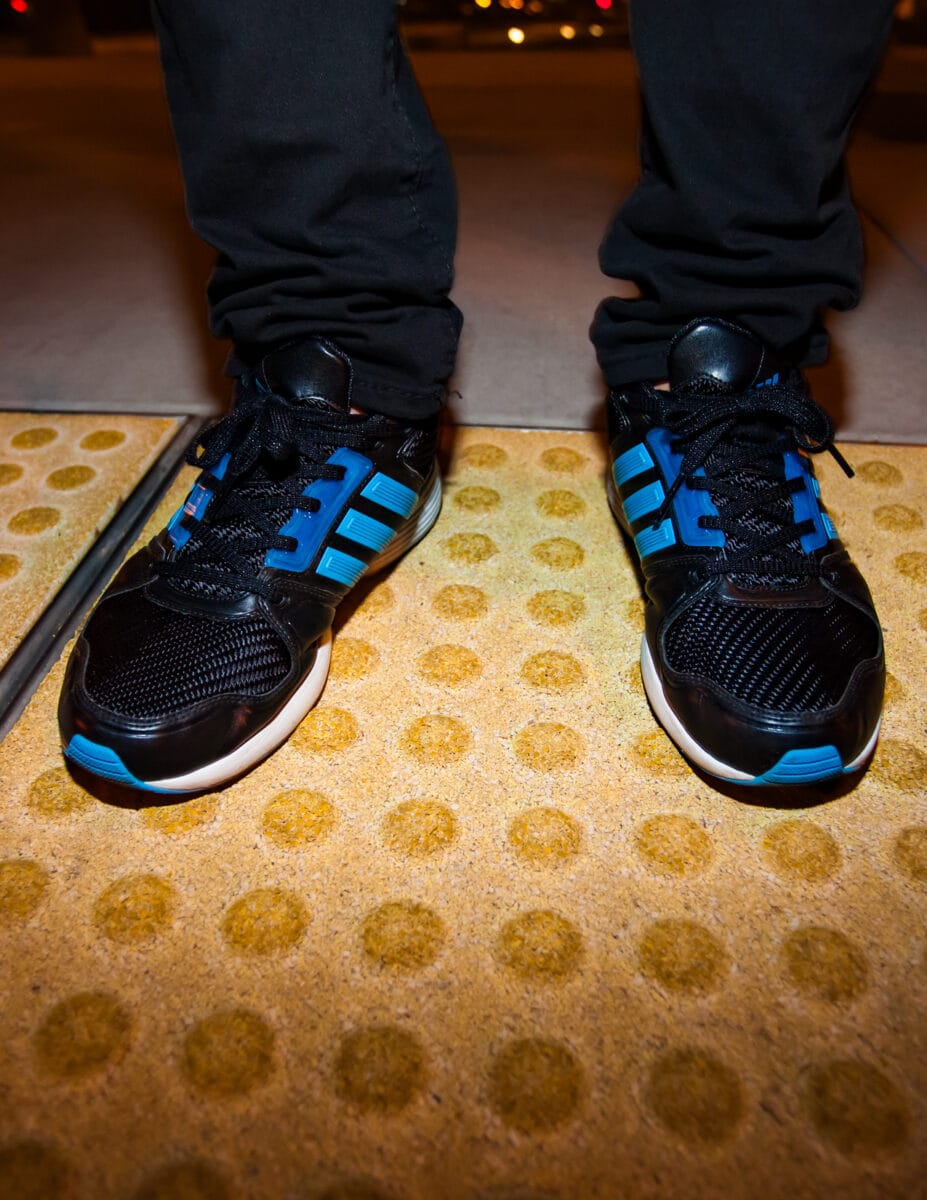 Adidas sneakers on foot at sidewalk crossing surface.